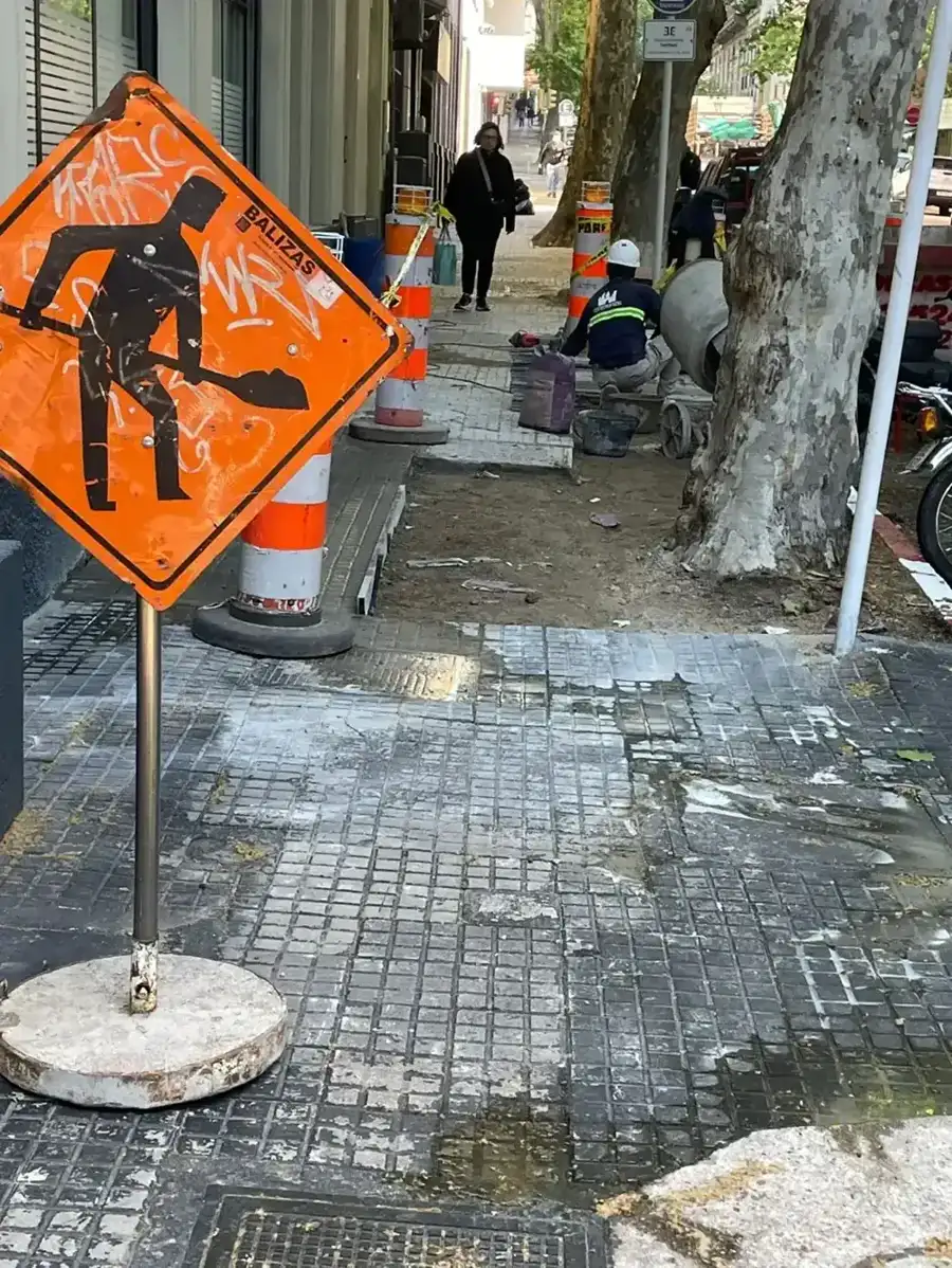 Cartel y conos de obra señalizando la reforma de vereda en la vía pública